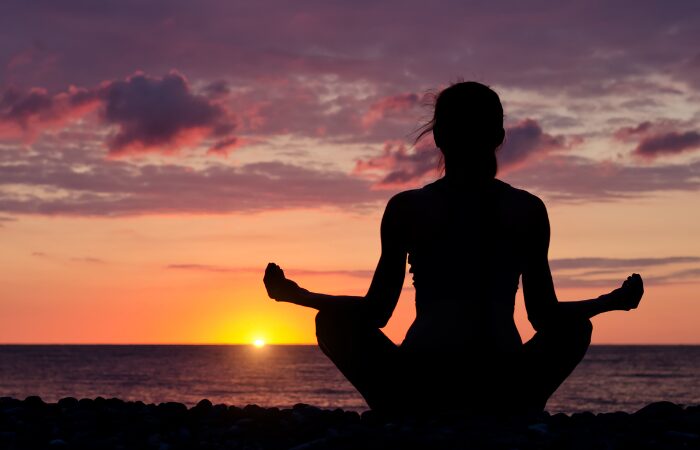How to do mindfulness for beginners 1 A woman at the beach in a mindfulness position on a sunset. How to do mindfulness for beginners