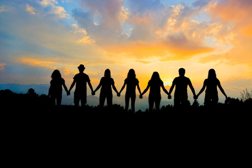 Group of strong people facing sunset in the mountain holding their hands.