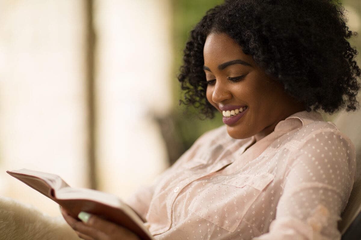 A black woman reading a book in a living room. How a simple shift in mindset can transform you life forever.