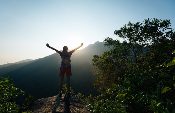 A woman hiker on top of a mountain facing the sunrise. 10 motivational quotes to start your day right