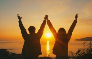 Strong young hikers at the top of the mountain confidently waving their arms in the air in a summer sunset. 9 Proven strategies to develop self-esteem